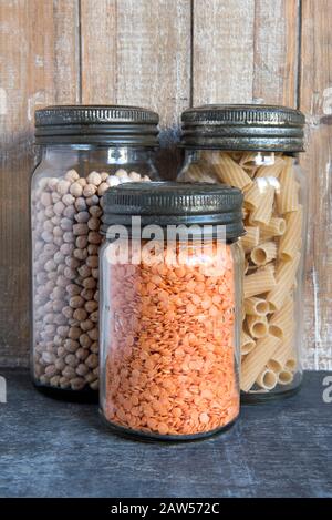 Vintage Kilner Glas Lagerung Lebensmittelgläser mit Metalldeckel mit roten Linsen, Kichererbsen und Pasta vor Holz Hintergrund in der Küche. Veganes, veganes, Null-Abfall-Konzept. Stockfoto