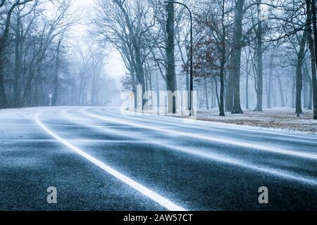 Die Straße ist von Bäumen umgeben, wenn der Schnee am schneebedeckten Wintertag fällt. Stockfoto