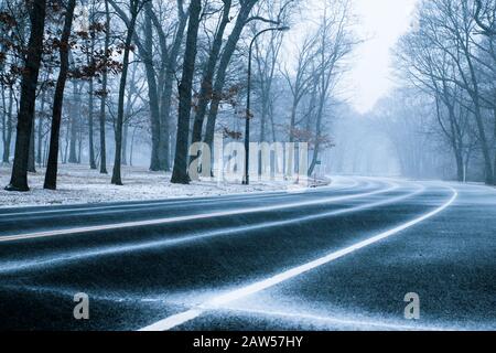 Die Straße ist von Bäumen umgeben, wenn der Schnee am schneebedeckten Wintertag fällt. Stockfoto