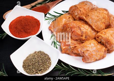 Rohes, rot gestepptes Huhn, Tomatenmarinade auf weißem Teller und Gewürzen. Stockfoto