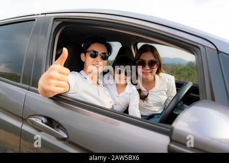 Die glückliche asiatische Familie mit dem Daumen nach oben und Mutter und Tochter tragen Sonnenschutzmittel im Kompaktwagen und lächeln und fahren auf Reisen im Urlaub. KFZ-Versicherung Stockfoto