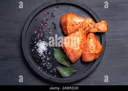 Rohe Hühnerbeine in Marinade mit Gewürzen auf schwarzem Teller. Eingelegtes rohes Fleisch. Stockfoto