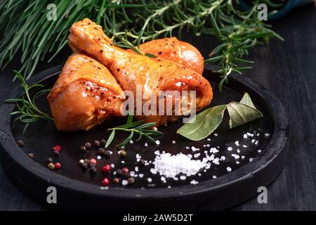 Rohe Hühnerbeine in Marinade mit Gewürzen auf schwarzem Teller. Eingelegtes rohes Fleisch.Draufsicht. Stockfoto