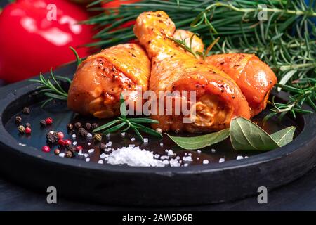 Rohe Hühnerbeine in Marinade mit Gewürzen auf schwarzem Teller. Eingelegtes rohes Fleisch. Stockfoto