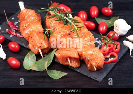 Rohe Hühnerspieße in Marinade mit Gewürzen auf schwarzem Teller und auf Holztisch. Rohe marinierte und würzige Hühnerspieße.Draufsicht. Hähnchenfleisch, Klo Stockfoto