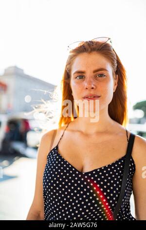 Junge Ingwerweibchen im trendigen Outfit, die an sonnigen Sommertag auf der Straße auf die Kamera blickt Stockfoto