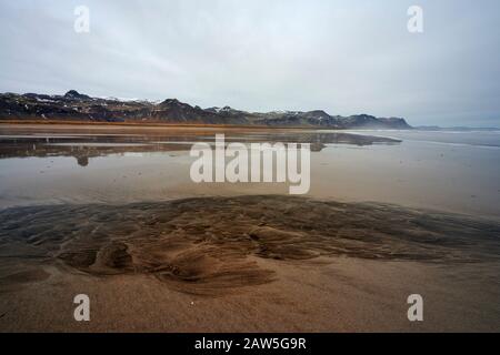 Algen wachsen auf sandigem Grund in transparentem Meerwasser in der Nähe der Bergkette an trübem Tag in der Natur Stockfoto