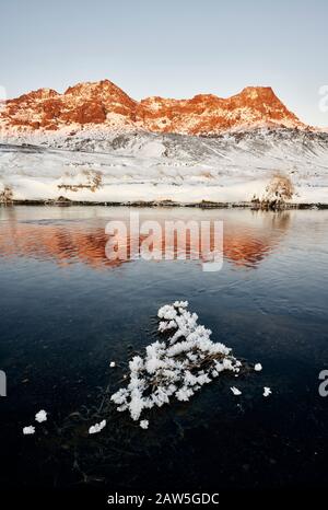 Landschaft des Sees in der Nähe von Steinufer gegen Berge mit Schnee im Winter bei Sonnenaufgang Stockfoto