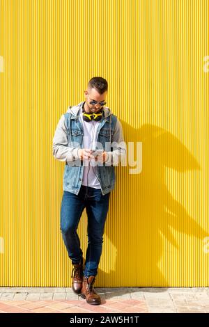 Porträt eines jungen, coolen Mannes über gelbem Hintergrund. Der Mann überprüft sein Handy. Stockfoto