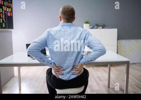 Junge Unternehmer mit Rückenschmerzen beim Sitzen im Büro Schreibtisch Stockfoto