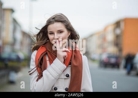 Sagen Sie niemandem, es ist unser Geheimnis. Frau fröhlich um Geheimhaltung bittet, vereinzelte Stille un fokussierte verschwommene Stadt auf den Hintergrund Stockfoto