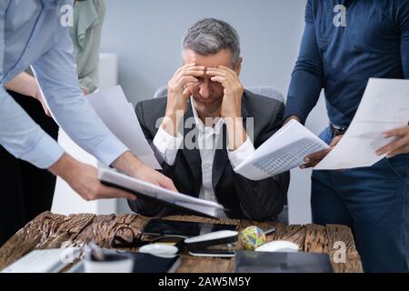 Betonte Unternehmer von seinen Kollegen mit Dokumenten in Office Umgeben Stockfoto