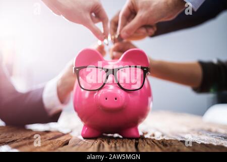Geschäftsleute, die sich an der Hand das Einwerfen von Münzen in rosa Sparschwein im Büro Stockfoto