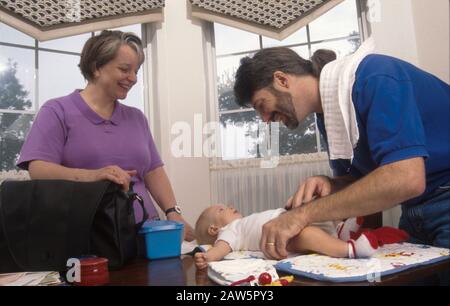 Bleib-zu-Haus-Papa ändert die Windel des dreimonatigen Jungen, während die Frau anschaut. Stockfoto