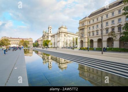 Touristen sehen am Kossuth-Parlamentsplatz, wie die ungarischen Regierungsgebäude im großen Spiegelbecken in Budapest, Ungarn, widerspiegeln. Stockfoto