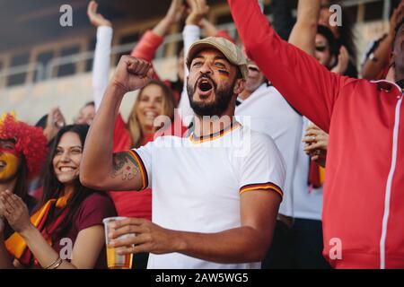 Zuschauer jubeln bei Sportveranstaltungen, ein Mann hält ein Glas Bier. Deutsche Fußball-Anhänger singen aktiv im Stadion. Stockfoto