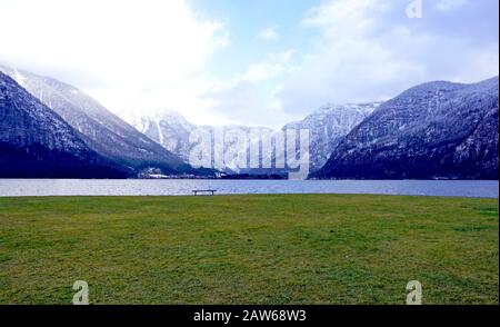 Panorama Hallstatter See und Grünrasenfeld im Freien und einsame Bank mit Schneeberghintergrund in Österreich in den österreichischen alpen Stockfoto