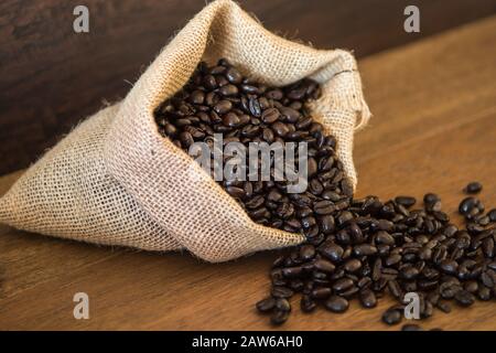 Gebratene Kaffeebohnen aus Jute-Bag auf Holzbrettern Stockfoto
