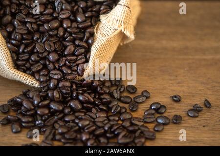 Gebratene Kaffeebohnen aus Jute-Bag auf Holzbrettern Stockfoto