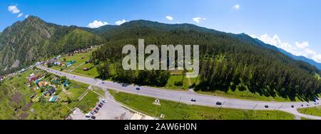 Ein weiter banner Luftblick auf die direkte Straße mit Autos in den Altai-Bergen, umgeben von grünem Wald und Bäumen. Stockfoto