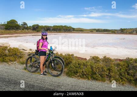 Ein Radfahrer posiert in einer heißen rosafarbenen Bluse vor dem Pink Lake auf Rottnest Island Stockfoto