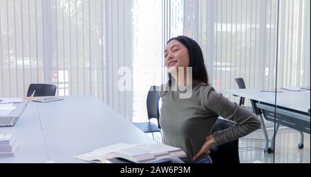 Asian Woman streckt sich nach dem Lesen des Buches und arbeitet hart und lächelt in der Bibliothek Stockfoto
