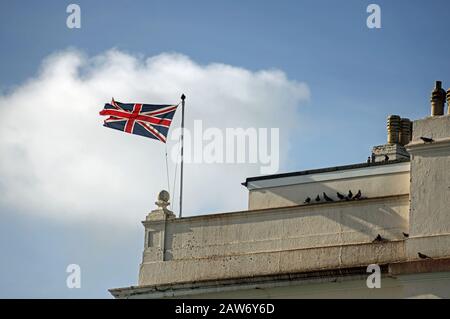 Am Ende einer Terrasse mit Gebäuden am Meer in Plymouth begrüßt eine gezotterte Flagge der Union Reisende, die in Millbay Docks, Plymouth, ankommen Stockfoto