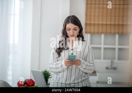 Langhaarige Frau in einer gestreiften Bluse, die eine Nachricht tippt Stockfoto