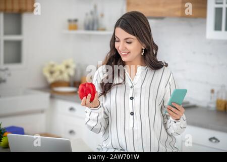 Langhaarige Frau in einer gestreiften Bluse, die einen roten Pfeffer hält Stockfoto