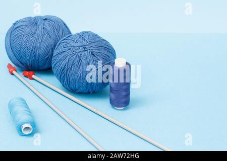 Strickgarnkugeln, Metallstricknadeln und Fäden auf blauem Grund. Strickkonzept. Stockfoto