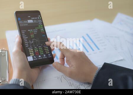 Geschäftsfrauen sitzen und analysieren die Börse am Telefon Der Hintergrund ist ein Aktiendiagramm Dokument Draufsicht Stockfoto