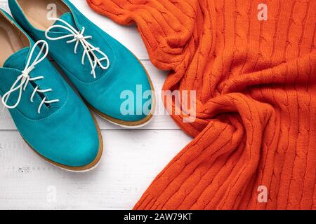 Ein Paar Aqua oxfords für Damen und ein orangefarbener Pullover auf weißem Holzhintergrund. Flaches, lässiges, trendiges Style-Konzept. Modebekleidung Stockfoto