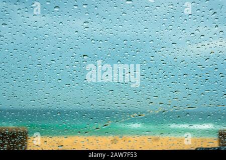 Nahaufnahme der Windschutzscheibe mit Regentropfen und Sandstränden im Hintergrund. Regenzeit Stockfoto