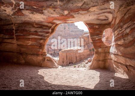 Natürliches Licht, das durch den Eingang eines Grabes in Petra eindringt, Jordanien in bunt geschichteten Sandsteinfelsen gehauen Stockfoto
