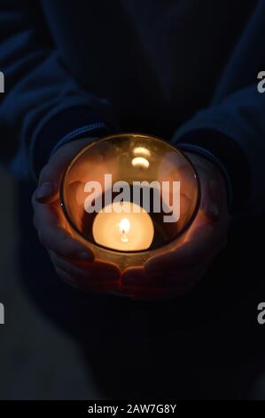 Hände von Kind um eine brennende Kerze im Dunkeln Stockfoto