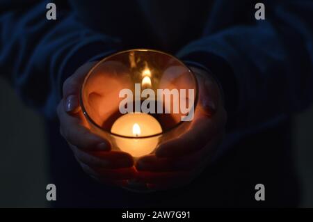 Hände von Kind um eine brennende Kerze im Dunkeln Stockfoto