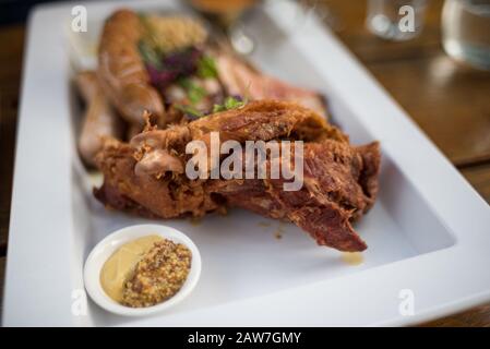 Nahaufnahme von gerösteten Schweinekoteletts mit Senfsamen, Sauce und Würstchen im Hintergrund Stockfoto