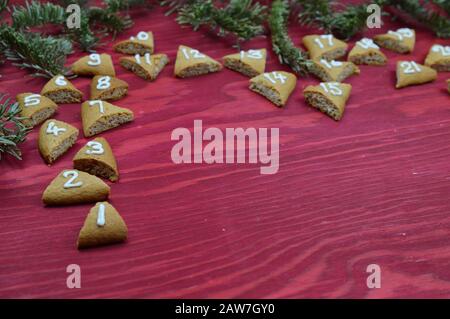 Vierundzwanzig nummerierte Adventskekse auf rotem Holz mit Kiefernägen Stockfoto