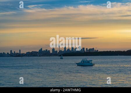 Farbenfroher Sonnenuntergang über dem Hafen mit Jachten und Sydey-Stadtbild, Silhouette in der Ferne Stockfoto