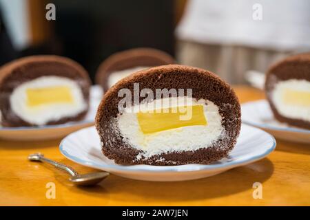 Köstliche Schokoladenkuchenrolle mit Sahne und Mango-Pudding. Aufgesetzte Schokoladenkuchenrolle. Stockfoto