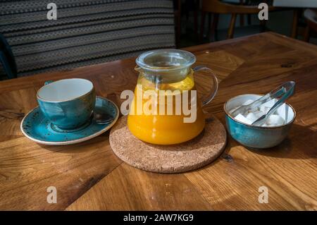 Orange-Sanddorn-Tee-Infusion in Glas-Teekanne mit Teelbecher und Zuckerschüssel mit Zuckerzange. Kräutermedikament Tee auf dem Tisch Stockfoto