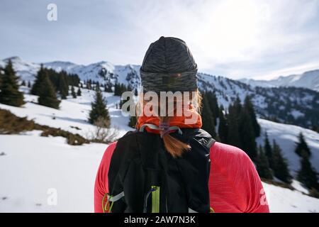 Die Frau des Trailläufers, die Berge auf Schnee betrachtet. Frau Athlet Läufer Rückansicht Stockfoto