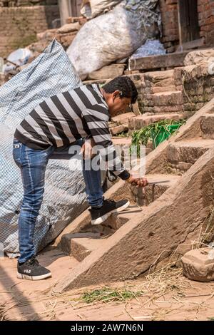 Ein Mann, der während des Bisket Jatra Festivals, Kathmandu-Tal, Nepal, Messer auf Steinstufen in Bhaktapur schärft Stockfoto