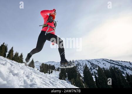 Die Frau des Trailers, die in den Winterbergen auf Schnee läuft. Dynamische Abfahrt auf der Spur Frau Athlet Runner Seitenansicht Stockfoto