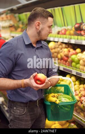 Mann kauft Obst im Supermarkt. Korb mit Bananen und Wassermelone, apfel in der Hand Stockfoto