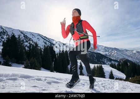 Die Frau des Trailers, die in den Winterbergen auf Schnee läuft. Dynamischer Lauf bergauf auf auf der Spur Frau Athlet Runner Seitenansicht Stockfoto