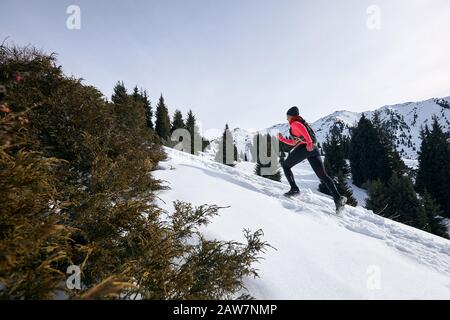 Die Frau des Trailers, die in den Winterbergen auf Schnee läuft. Dynamischer Lauf bergauf auf auf der Spur Frau Athlet Runner Seitenansicht Stockfoto