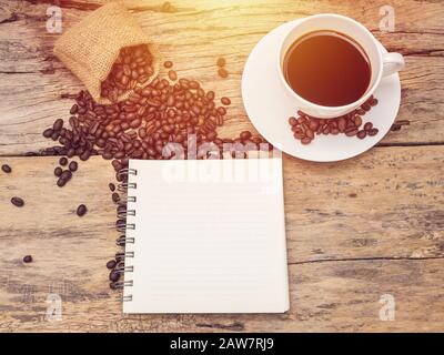 Heiße Kaffeetasse mit Kaffeebohne und Notizbuch auf Holztisch. Kaffee Hintergrundmenü für Café oder Café-Bar Stockfoto