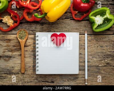 Flach von leeren Rezept kochen Buch und Utensilien mit Kräutern und bunten Paprika über Holz- Hintergrund. Ansicht von oben mit der Kopie Raum. Essen Rezept ein Stockfoto