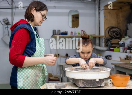 Ein 6-jähriges Mädchen lernt, mit einem Weib Töpfer an einem Töpferrad zu arbeiten.Meisterklasse in einer Töpferwerkstatt Stockfoto